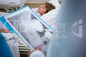 Patient lying on bed while doctor holding medical report