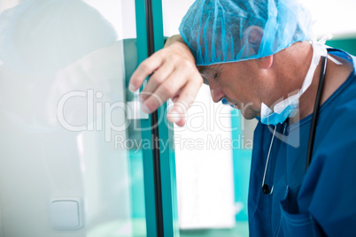 Sad surgeon leaning against the glass door