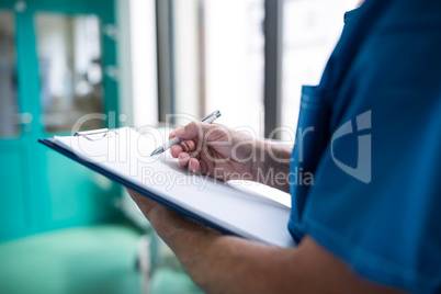 Mid section of surgeon writing on clipboard in corridor