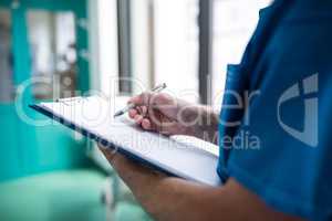 Mid section of surgeon writing on clipboard in corridor