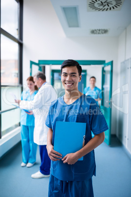 Smiling male surgeon holding a clipboard in corridor