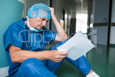 Sad surgeon sitting on floor with report in corridor