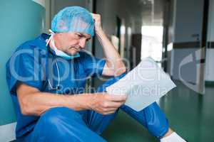 Sad surgeon sitting on floor with report in corridor