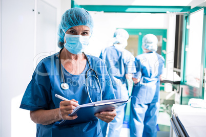 Female surgeon writing on clipboard in corridor