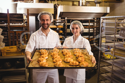 Portrait of female and male baker holding a tray of michetta