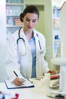 Pharmacist standing at counter and writing on clipboard