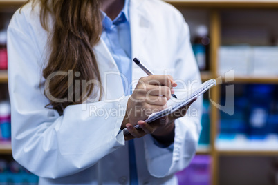 Pharmacist writing on notepad in pharmacy