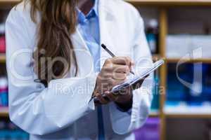 Pharmacist writing on notepad in pharmacy