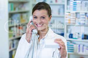 Pharmacist holding medicine box while talking on phone in pharma