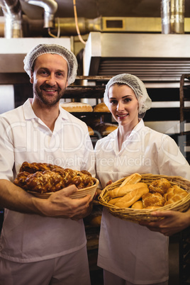 Portrait of female and male baker holding basket of bread and sw