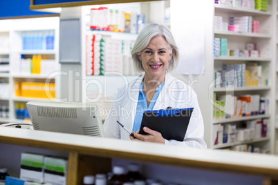 Smiling pharmacist holding a clipboard in pharmacy