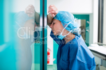 Sad surgeon leaning against the glass door