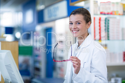 Smiling pharmacist sitting at counter in pharmacy