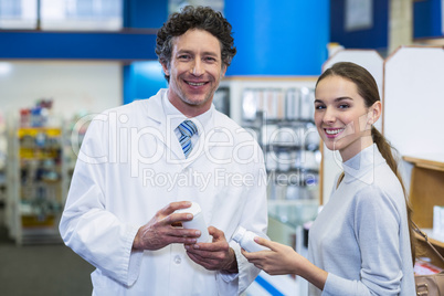 Smiling customer and pharmacist holding drug bottle in hospital