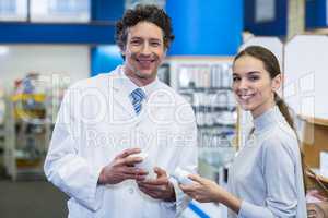 Smiling customer and pharmacist holding drug bottle in hospital