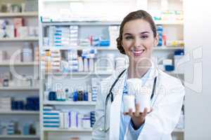 Smiling pharmacist showing medicine container in pharmacy