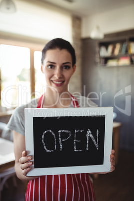 Portrait of female baker holding open signboard