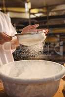 Mid-section of female baker sifting flour through a sieve