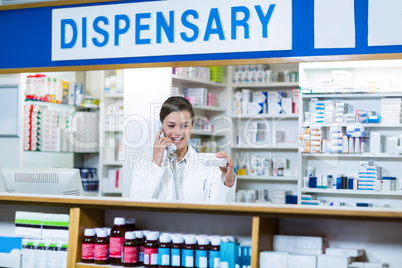 Pharmacist looking at medicine box while talking on phone