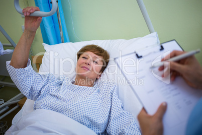 Patient lying on bed while nurse writing on clipboard