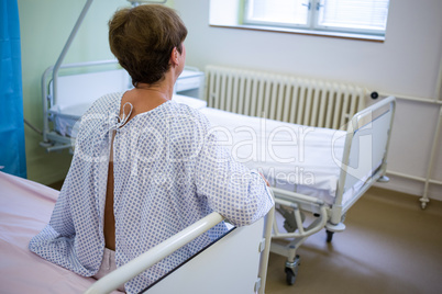 Rear view of sad senior patient sitting on a bed