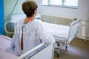 Rear view of sad senior patient sitting on a bed