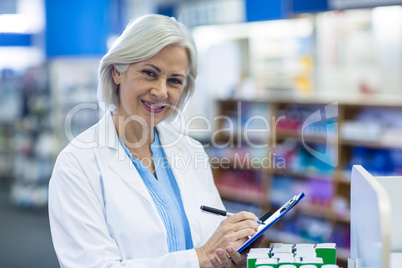 Pharmacist writing on clipboard in pharmacy