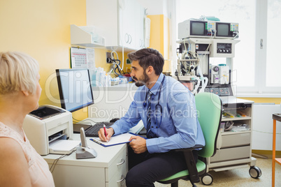 Doctor writing on clipboard while looking at computer