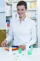 Smiling pharmacist putting pill in container at pharmacy