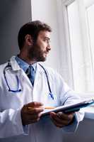 Doctor looking through window while holding clipboard
