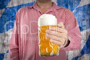 Man in traditional Bavarian shirt holds mug of beer