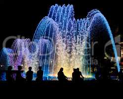 Night colored fountain with silhouettes of people.