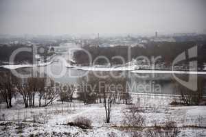 Winter landscape of snow-covered fields, trees and river in the early misty morning