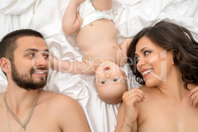 Top view of happy young family posing lying in bed