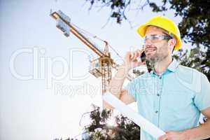 Composite image of male architect with blueprint talking on mobile phone
