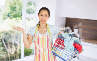 Composite image of puzzled young woman holding laundry basket full of dirty laundry