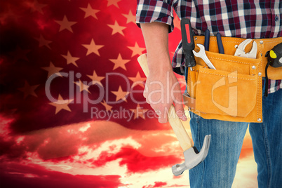Composite image of repairman wearing tool belt while holding hammer