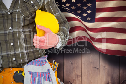 Composite image of manual worker wearing tool belt while holding helmet