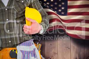 Composite image of manual worker wearing tool belt while holding helmet