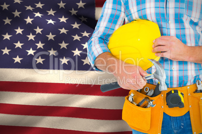 Composite image of manual worker wearing tool belt while holding hammer and helmet