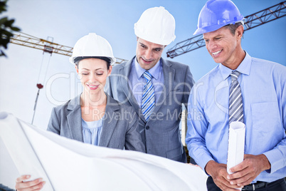 Composite image of businessmen and a woman with hard hats and holding blueprint