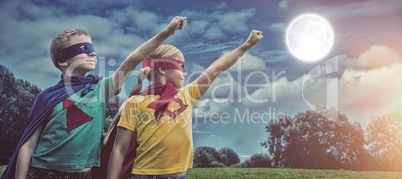 Composite image of siblings in capes standing with hands raised