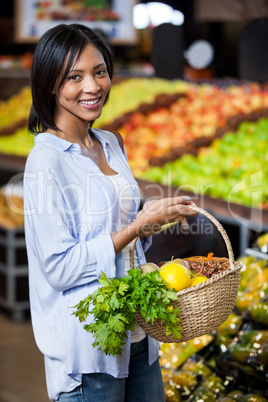 Smiling woman holding fruits and vegetables in basket