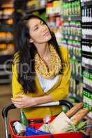 Thoughtful woman standing with shopping cart in grocery section