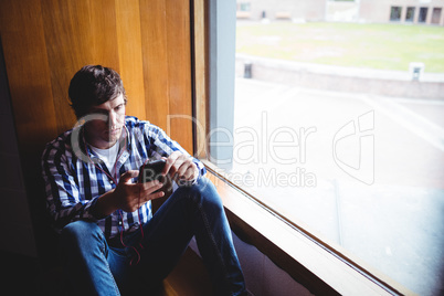 Student using mobile phone near window