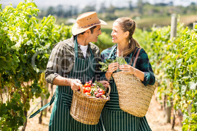Happy farmer couple holding baskets of vegetables