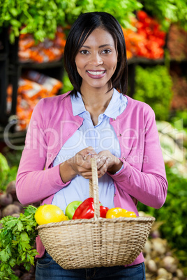 Smiling woman holding fruits and vegetables in basket