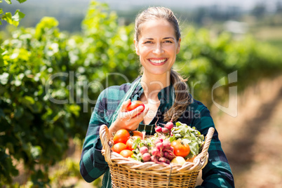Portrait of happy female farmer holding a basket of vegetables