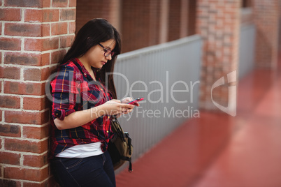 Female student using mobile phone in corridor