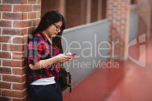 Female student using mobile phone in corridor